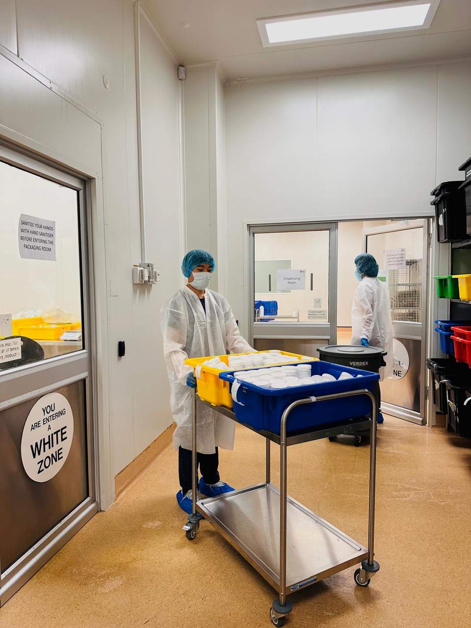 Gowned and capped staff moving a trolley through the GMP area