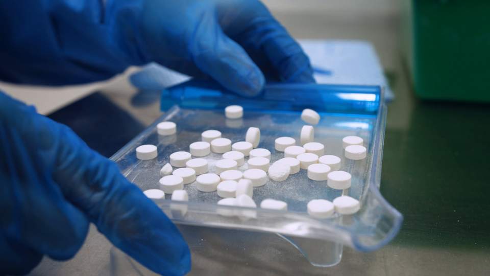 Gloved hands arrange tablets on a counting tray