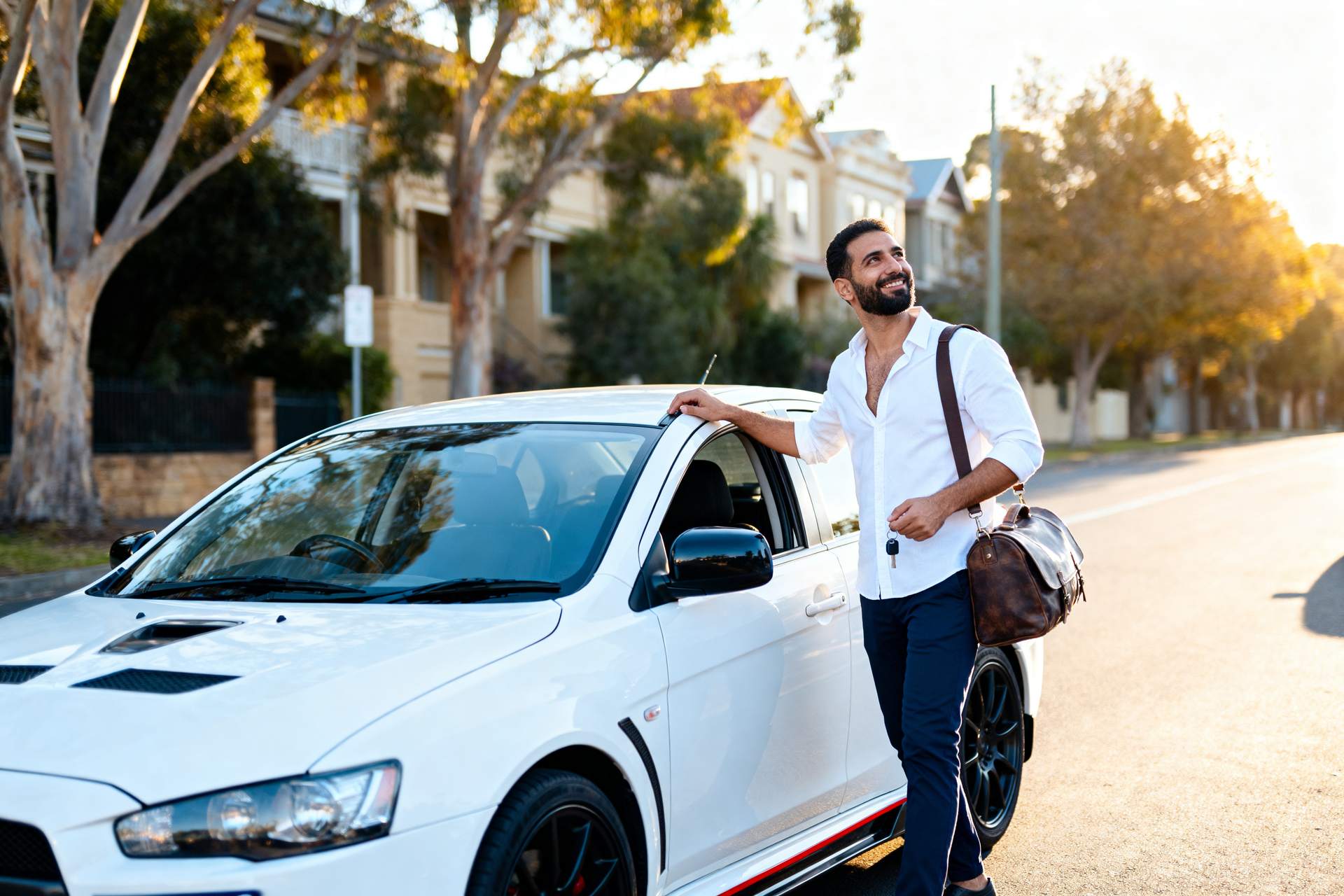 A man opening the driver's door of a white sedan on a sunny street